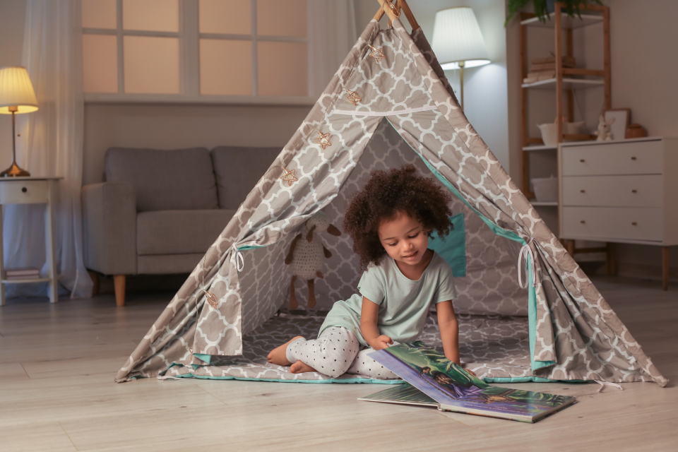 A child smiling while reading a book in a play tent